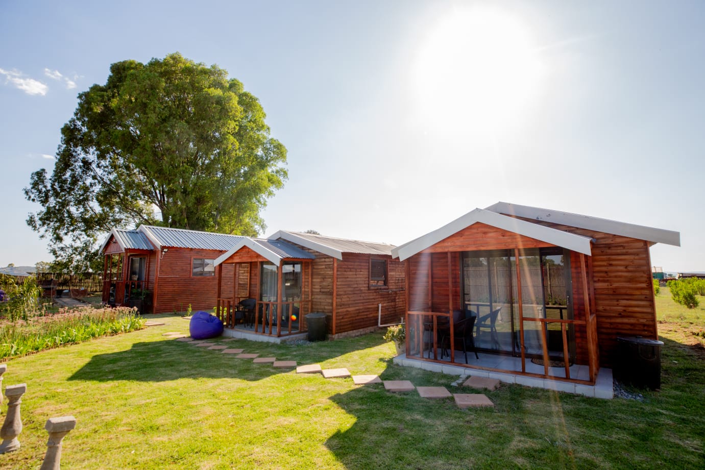 Wooden cabins surrounded by green lawns, garden paths, and open outdoor space for a peaceful countryside stay.